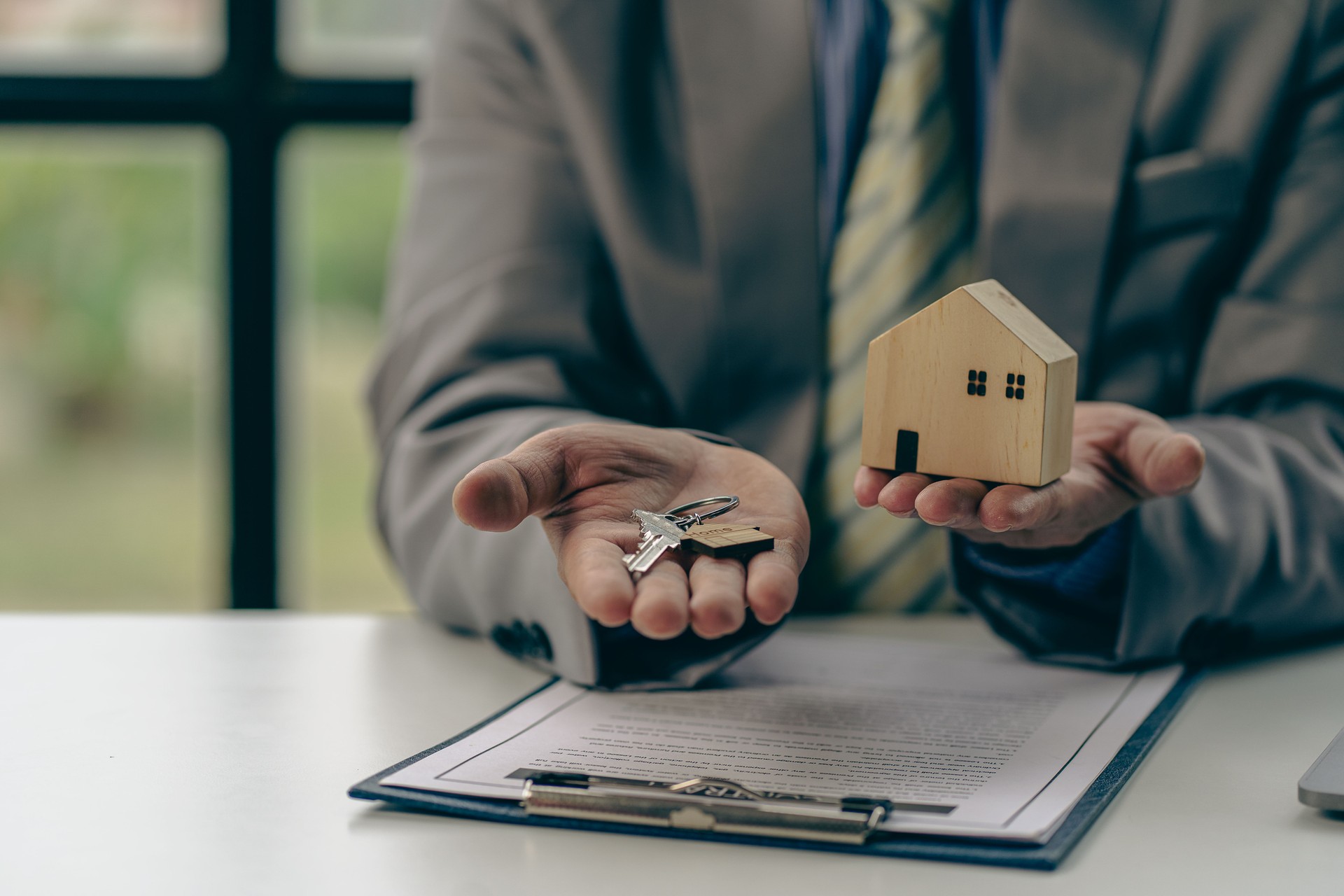 Businessman holding keys and handing over house to customer, real estate agent handing over keys to home buyer after contract of purchase